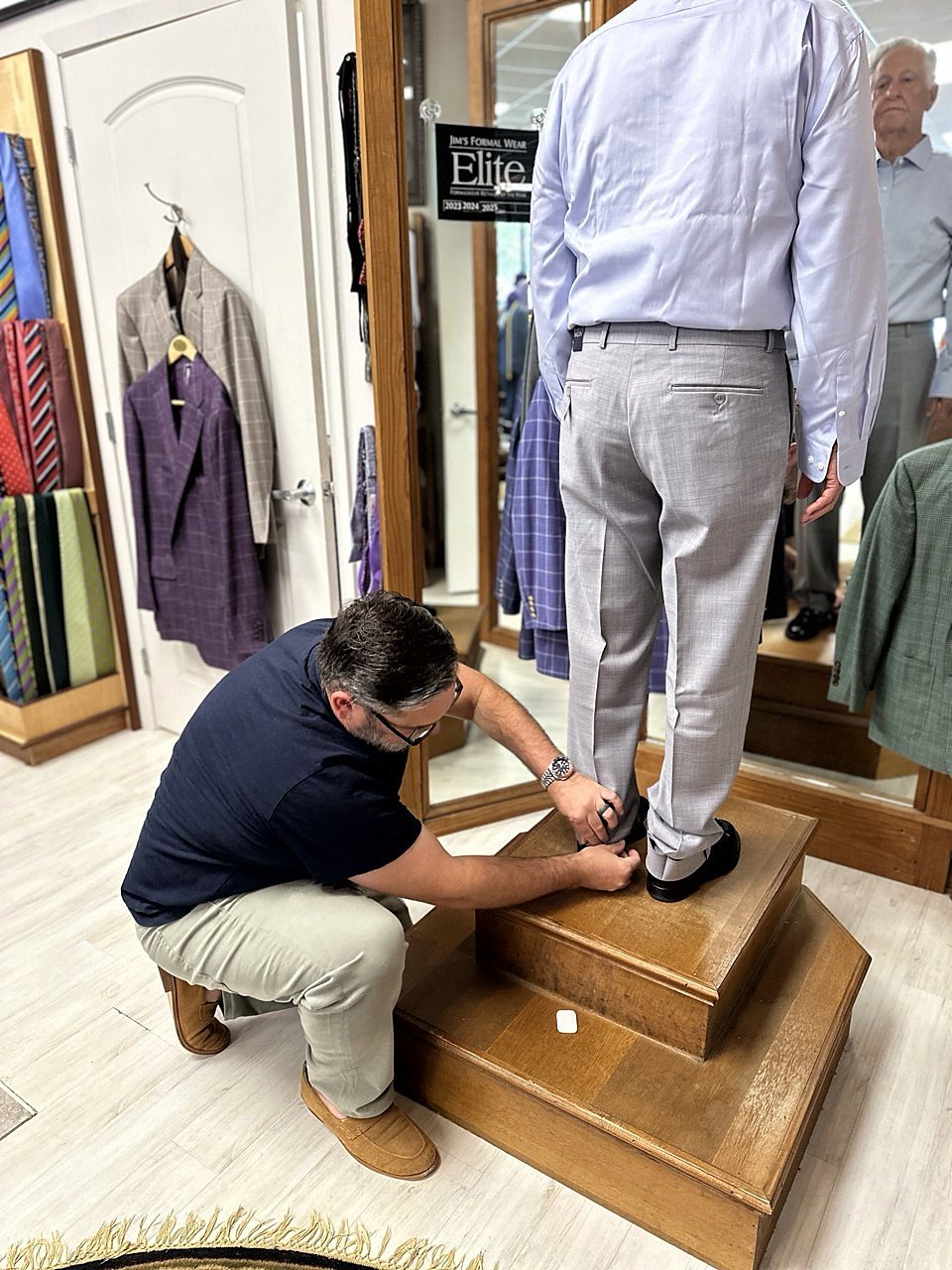 A tailor pinning trouser hems on the fitting platform at Harper's